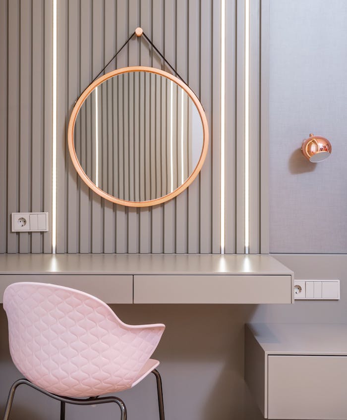 Stylish empty vanity table under round mirror on wall near light pink armchair in stylish bedroom